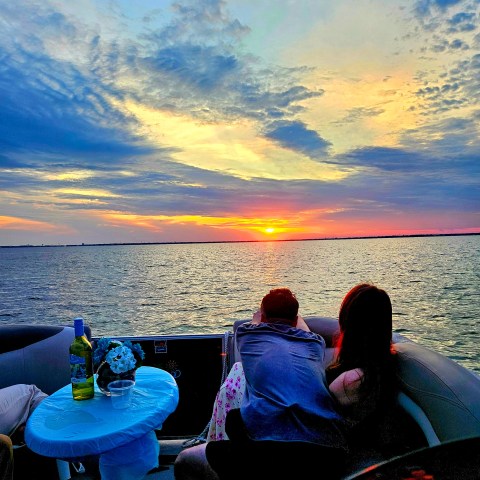 Couple on a boat watching a vibrant sunset over the ocean.