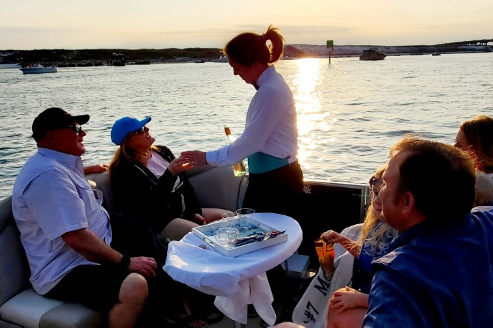 People relaxing on a boat with drinks at sunset, served by a staff member.
