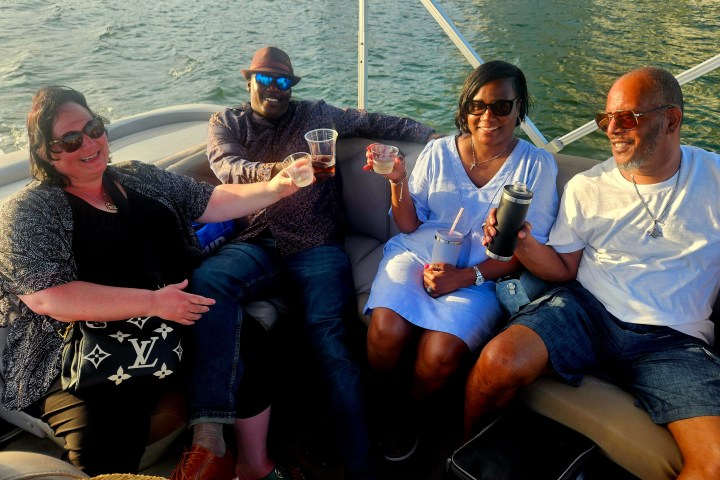 Four people smiling and holding drinks on a boat.