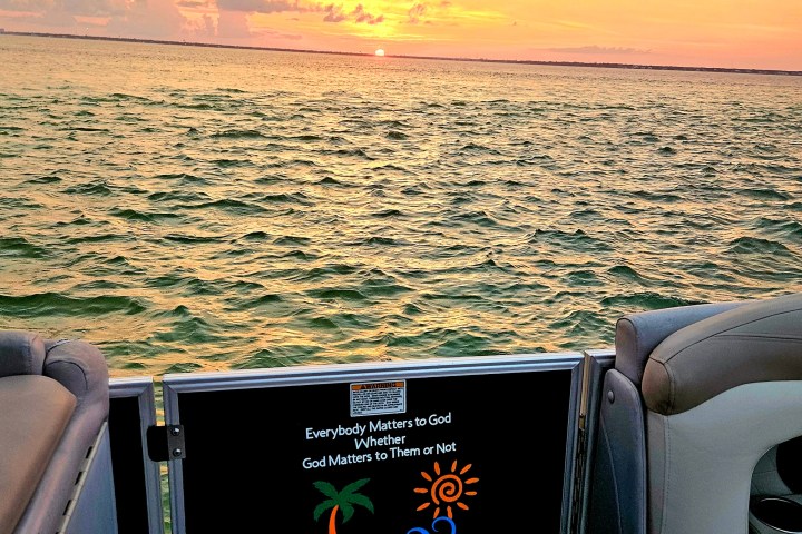 Sunset view from a boat with water and a slogan on the railing.