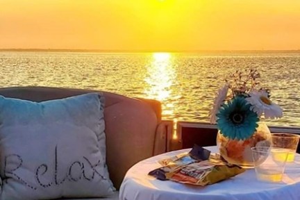 Sunset over water, sofa with 'Relax' cushion, table with snacks and drinks.