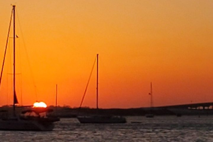 Sailboats on water at sunset with a bridge in the background.