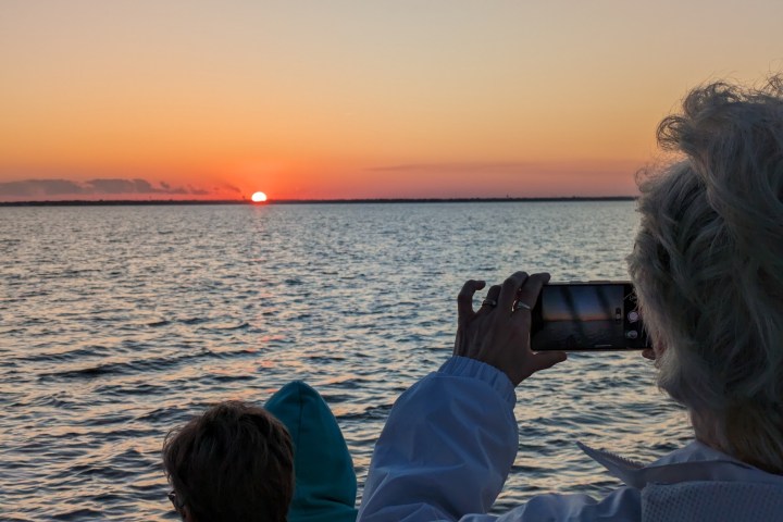 People watch and photograph a sunset over a calm sea.