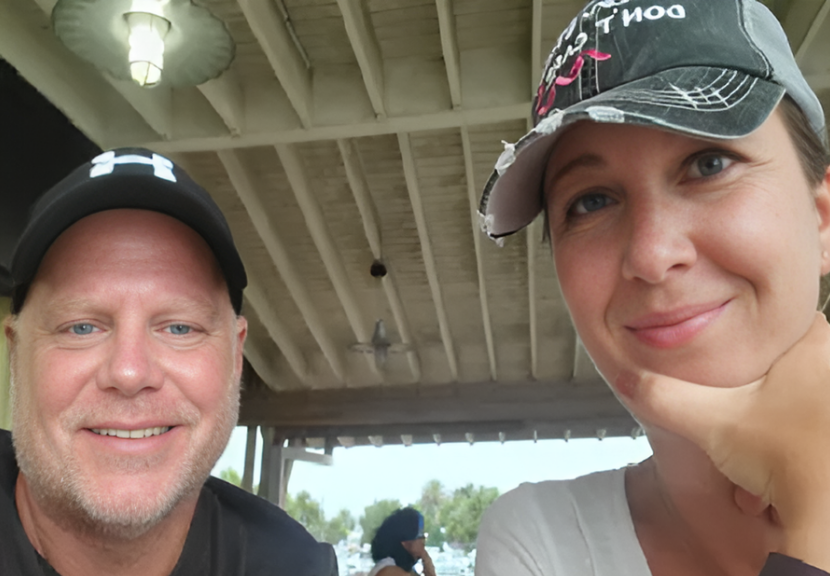 Two people smiling under a wooden roof, with ceiling fans and lights visible.