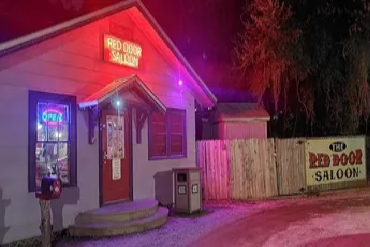 Small building with red neon sign 'Red Door Saloon' at night.