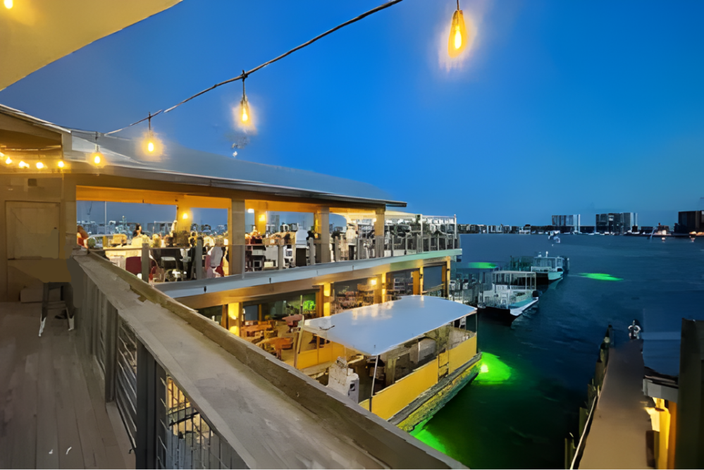 Rooftop restaurant by waterfront at dusk with string lights.